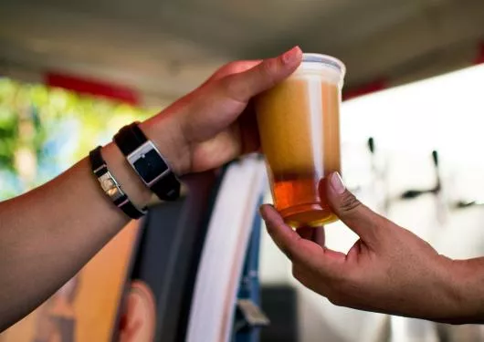 Een plastic beker met bier wordt van de ene hand in de andere hand doorgegeven.