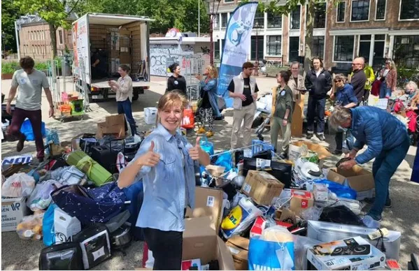 vrouw staat met 2 duimen omhoog tussen afgedankte spullen op een plein