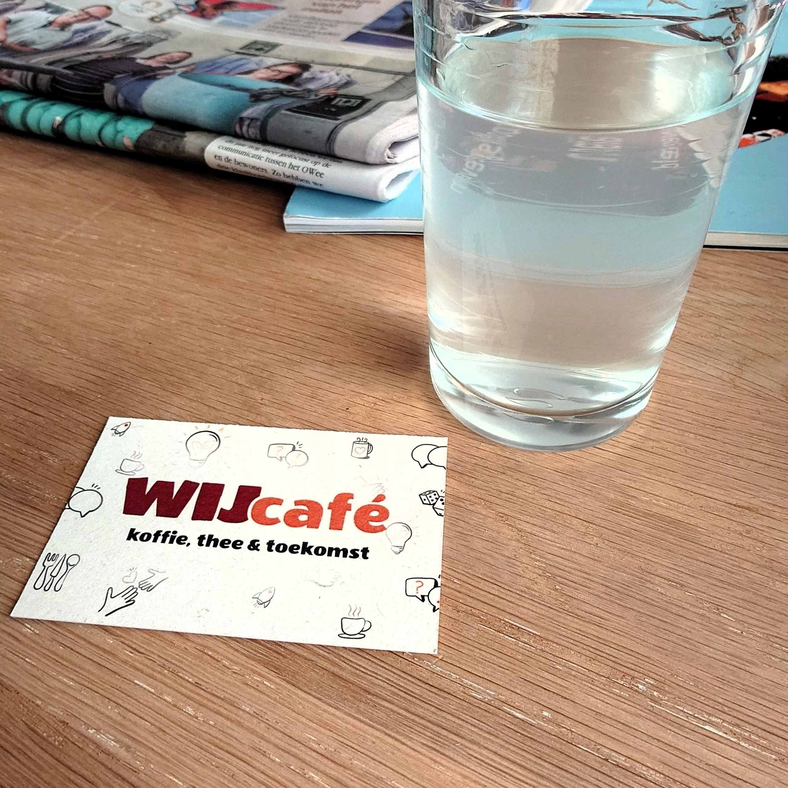 cafétafel met visitekaartje 'WIJcafé' en glas frisdrank